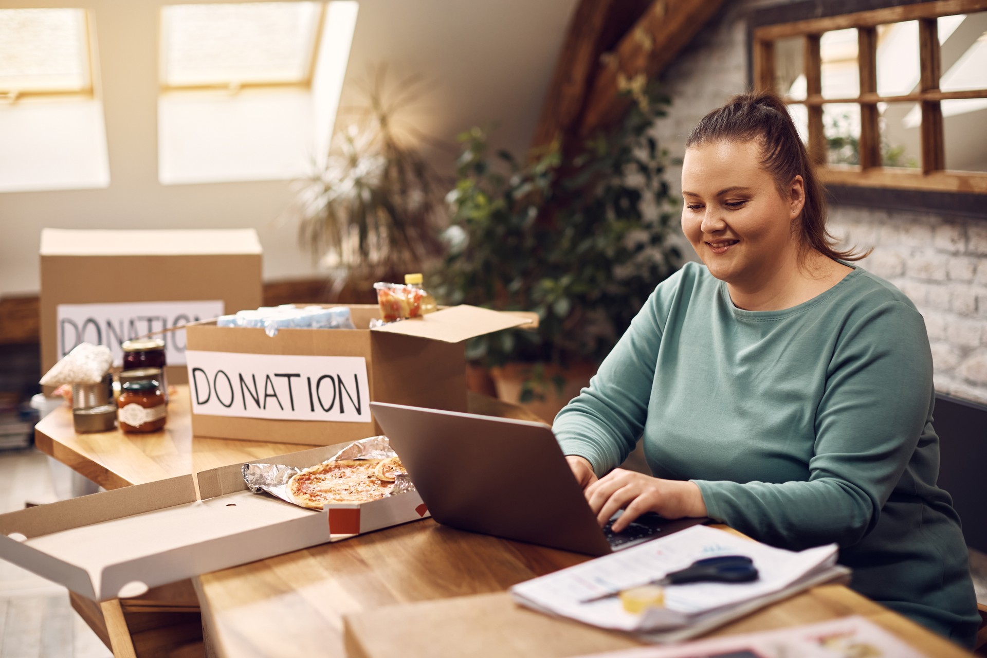 Happy woman working on laptop while organizing donation boxes.